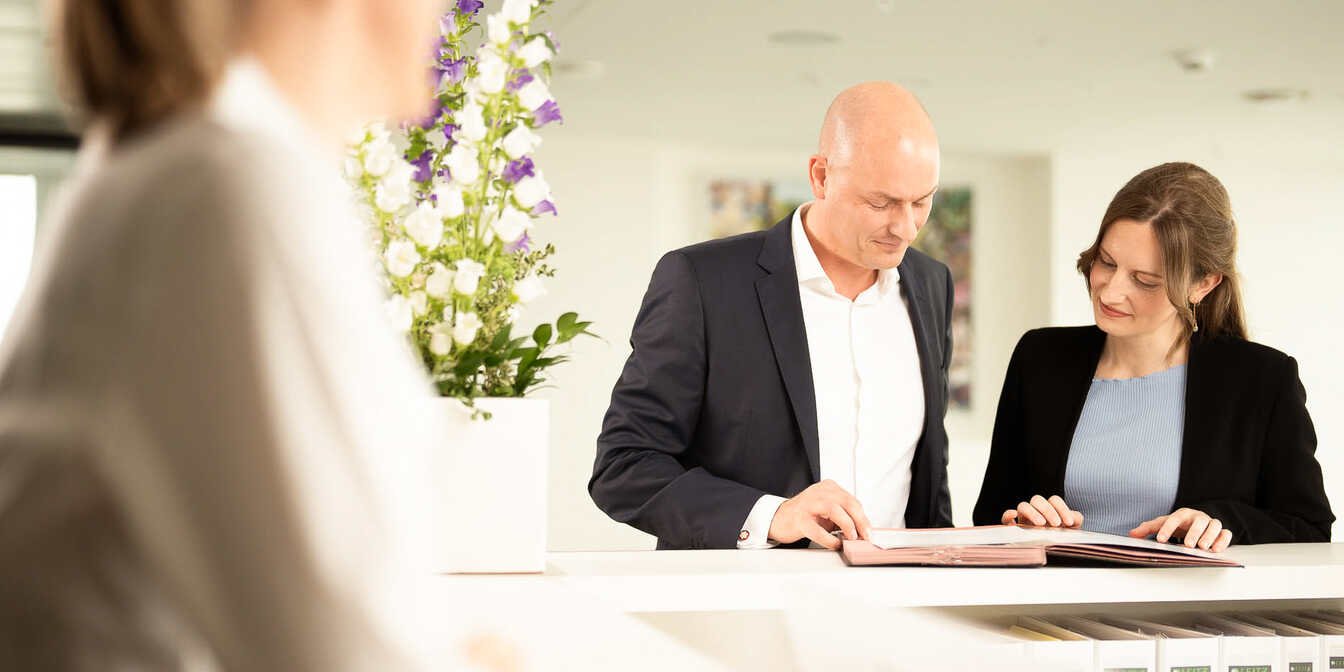 Eine Anwältin und ein Anwalt stehen an einer Theke mit Akten vor ihnen