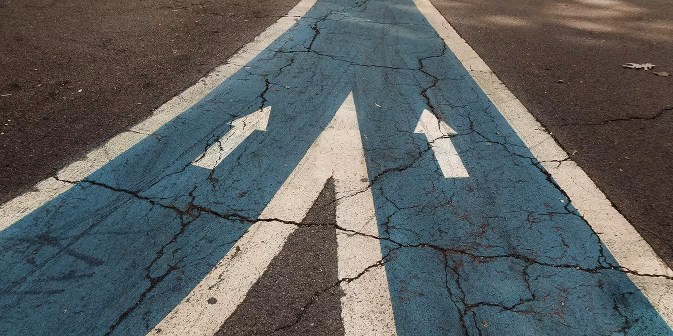 Straße mit zwei Pfeilwegen die zusammenführen zu einem Weg 