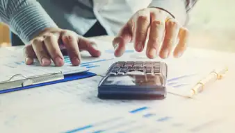 Hand, die einen Taschenrechner benutzt und Unterlagen auf dem Tisch