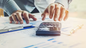 Hand, die einen Taschenrechner benutzt und Unterlagen auf dem Tisch