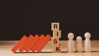 Eine Mauer in der Mitte die Risk abbildet, die die roten Steine auf der linken Seite aufhält auf die Modellmännchen auf der anderen Seite zu fallen. 